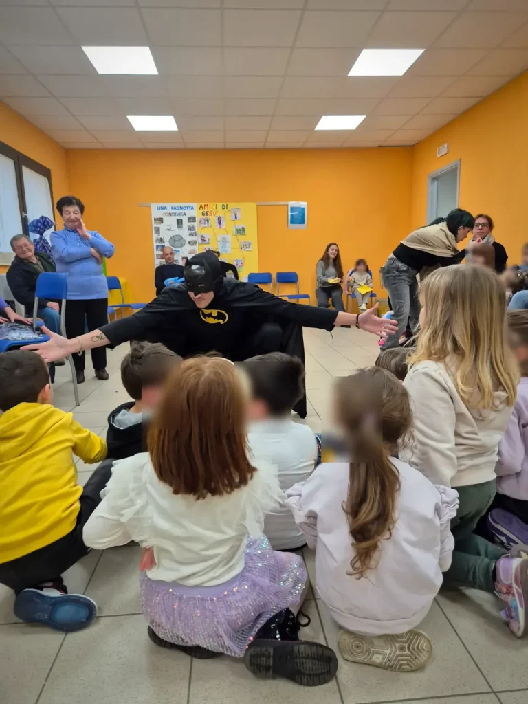 Batman entra nella sala e i bambini seduti in cerchio lo accolgono