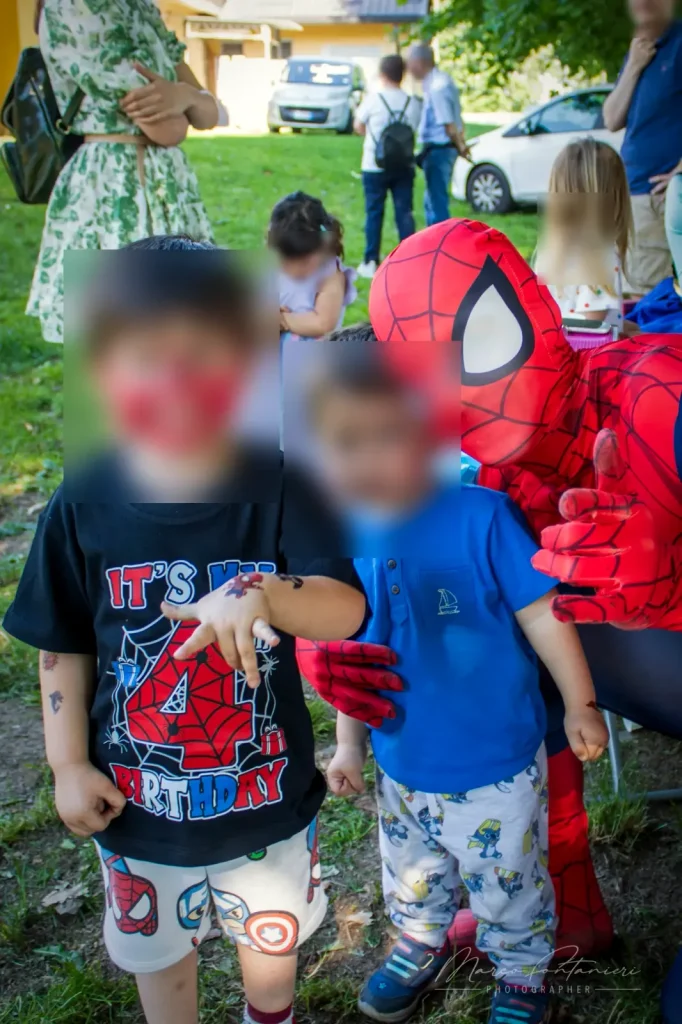 Due bambini con il trucco di Spiderman sul viso, e Spiderman dietro di loro al parco