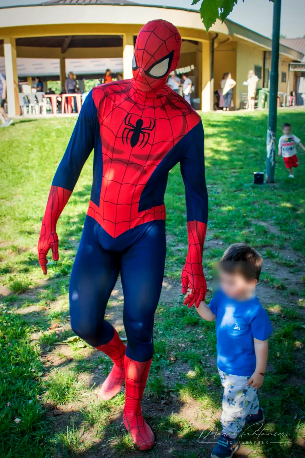 Spiderman cammina sul prato tenendo per mano un bambino